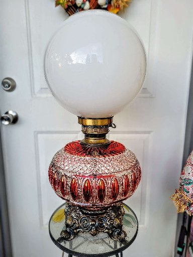 Electrified cranberry glass lamp with ornate cast metal cherub base and white globe shade