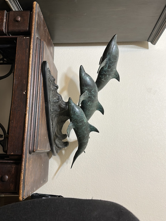 Bronze sculpture depicting three dolphins leaping over ocean waves