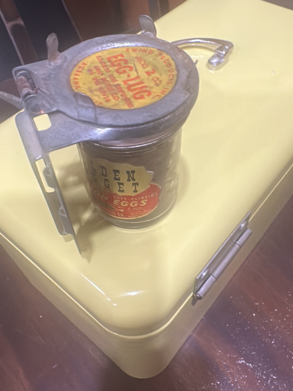 Glass jar with metal hand-crank nut grinder attachment labeled 'Don't Fret Shelled Eggs'