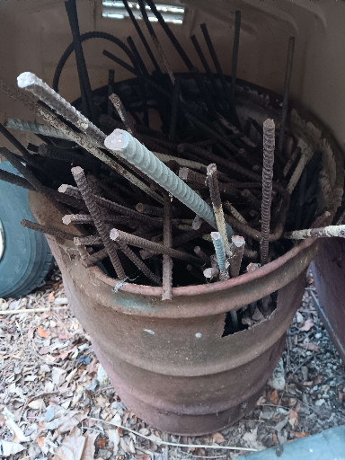 Collection of vintage rusted rebar (reinforcing bar) and metal rods in aged metal bucket
