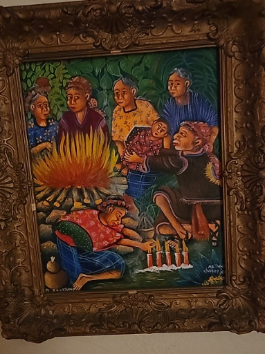 Acrylic painting on canvas depicting a Guatemalan or Central American family scene around a fire, framed in ornate gilded wood