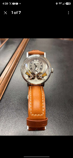 Stainless steel mechanical watch with visible balance wheels and tan leather strap