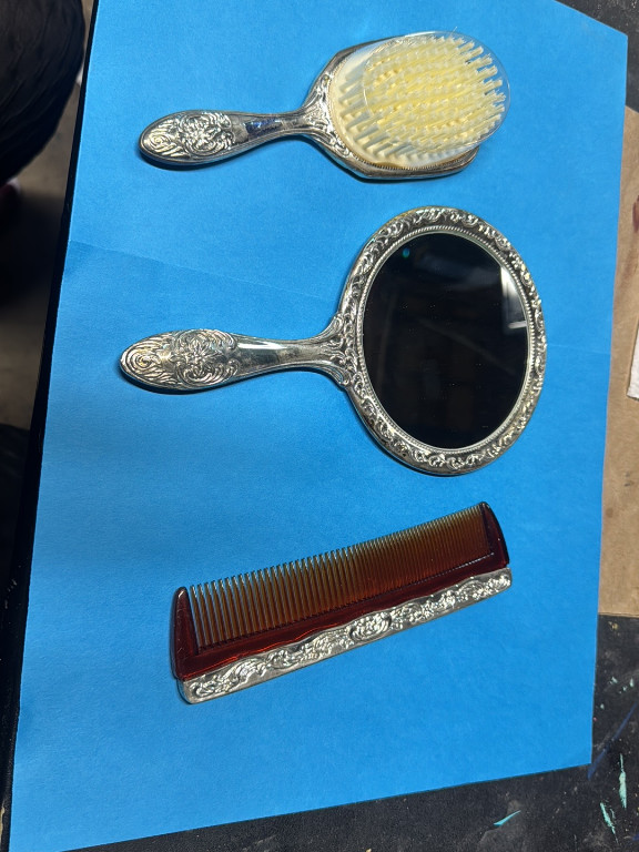 Silver-plated vanity set including hand mirror, hairbrush, and comb with ornate floral repousse pattern