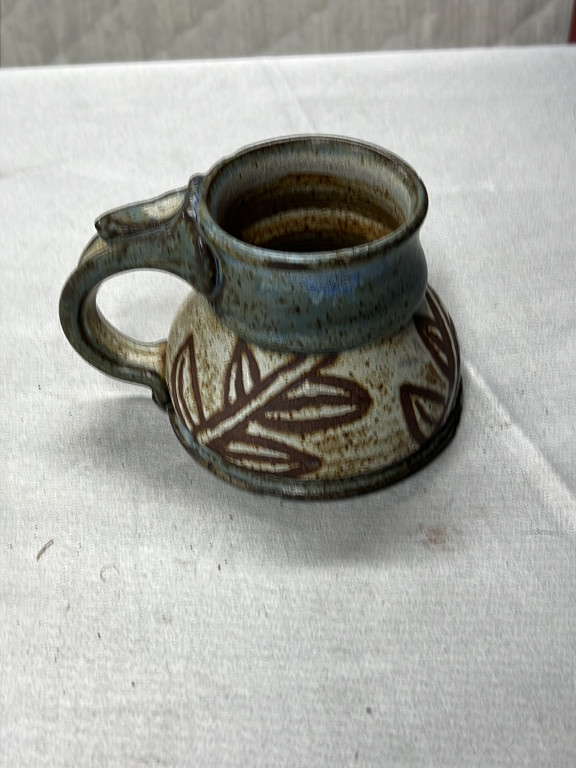 Handmade stoneware pottery mug with carved leaf design and blue-green glaze