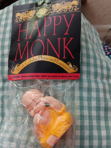 Plastic novelty figurine titled 'Happy Monk' with cellular phone and espresso