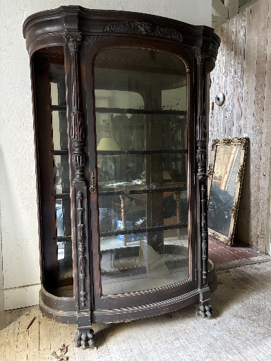 Quarter-sawn oak curved-glass curio cabinet with carved figural details and claw feet