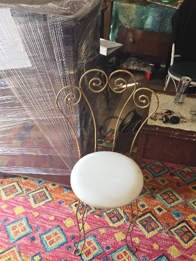 Mid-century metal vanity stool with white vinyl upholstered seat and decorative scrollwork backrest