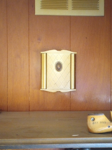 Decorative wall-mounted chime or doorbell cover in cream enamel and brass