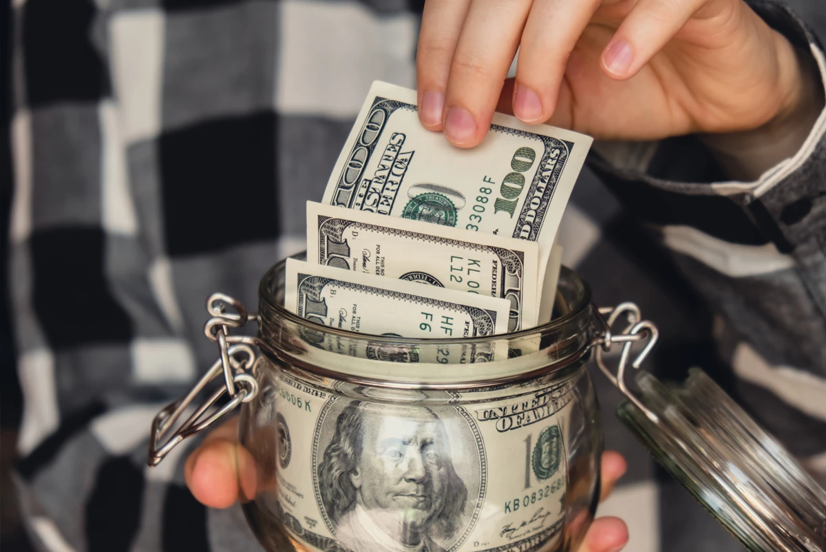 Hands placing dollar bills into a savings jar