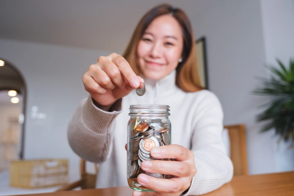 Woman adding coin to savings jar