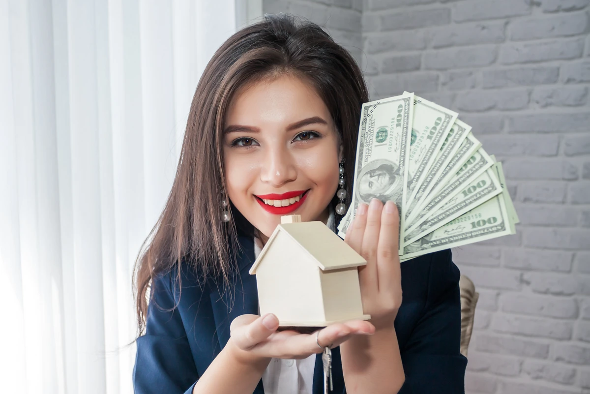 Woman holding house model and cash.