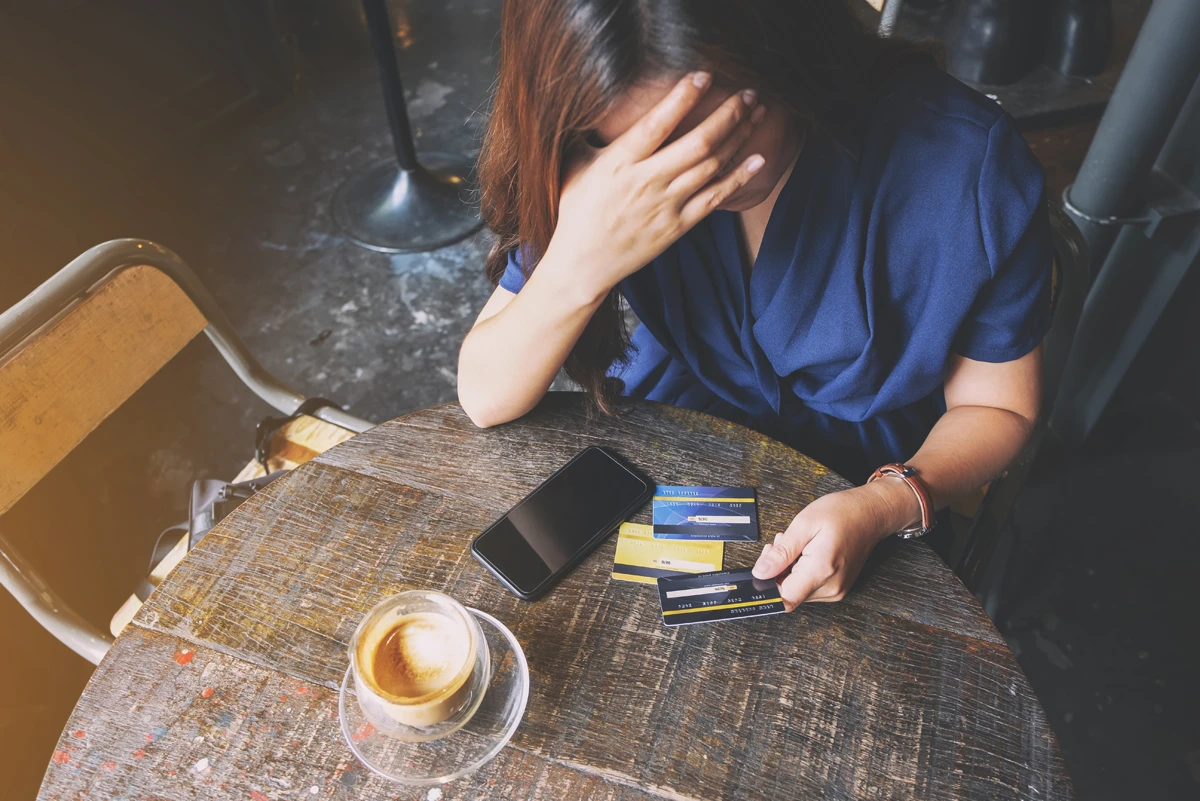 Stressed woman with credit cards and phone at cafe.