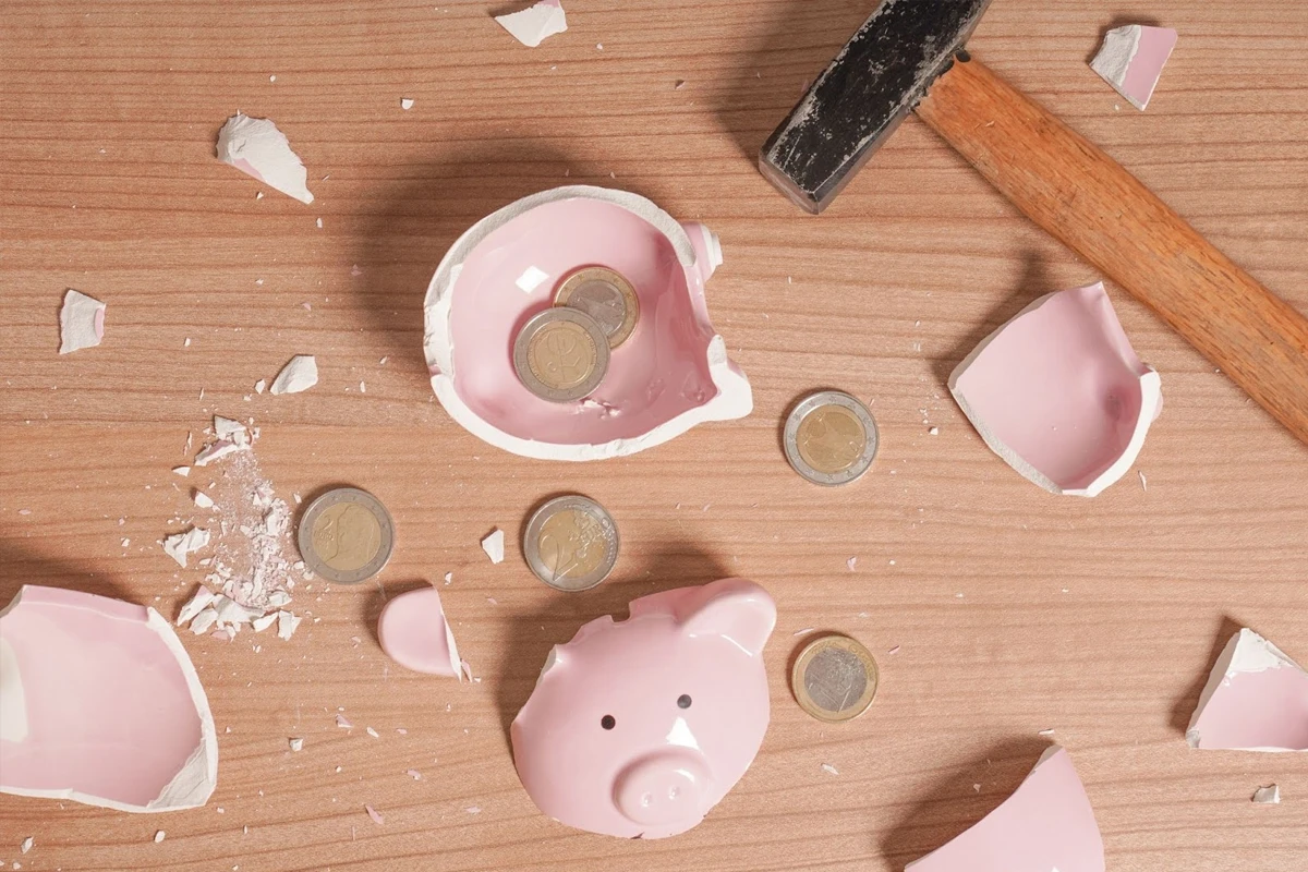 Broken piggy bank with coins and hammer on table