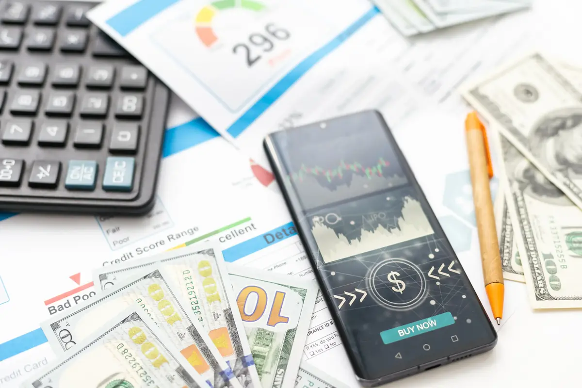 Smartphone displaying a financial app with a "Buy Now" button, surrounded by cash, a calculator, and credit score documents.