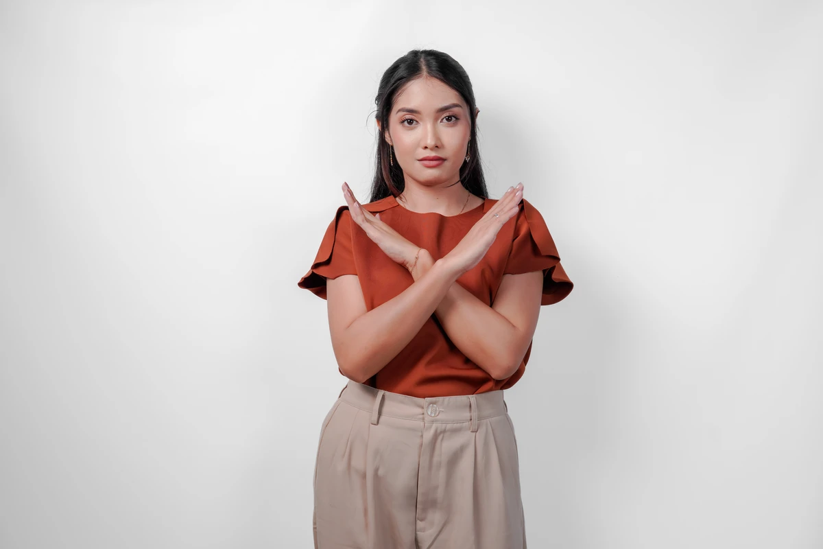 Woman in rust top gesturing 'no' with crossed arms