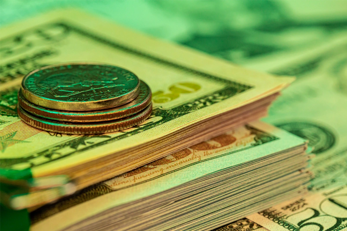 Stacked U.S. currency and coins in green light