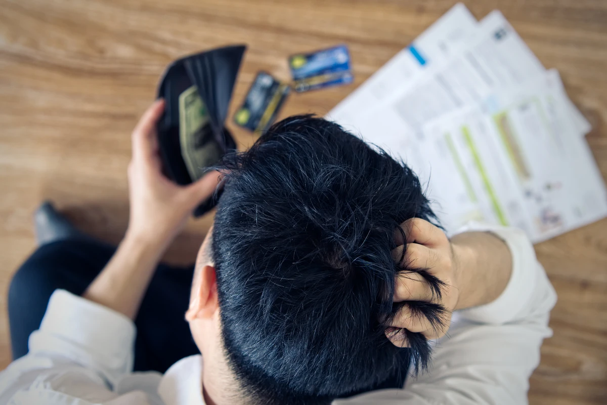 Person holds an open wallet containing cash, surrounded by credit cards and bills, suggesting financial stress or payment concerns.