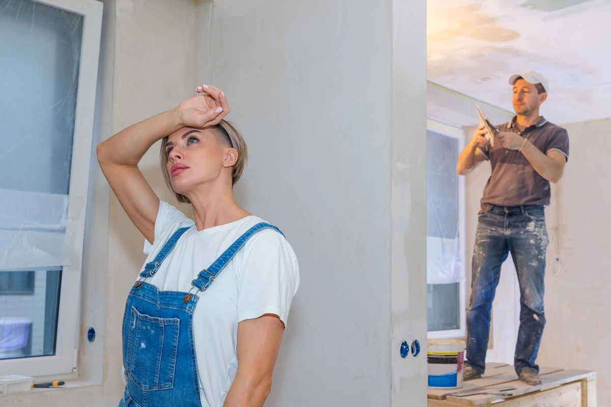 Woman stressed during home renovation, man works in background