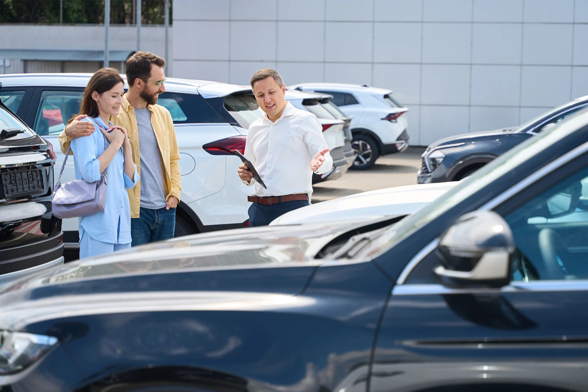 Couple comparing used cars with a salesperson at a dealership