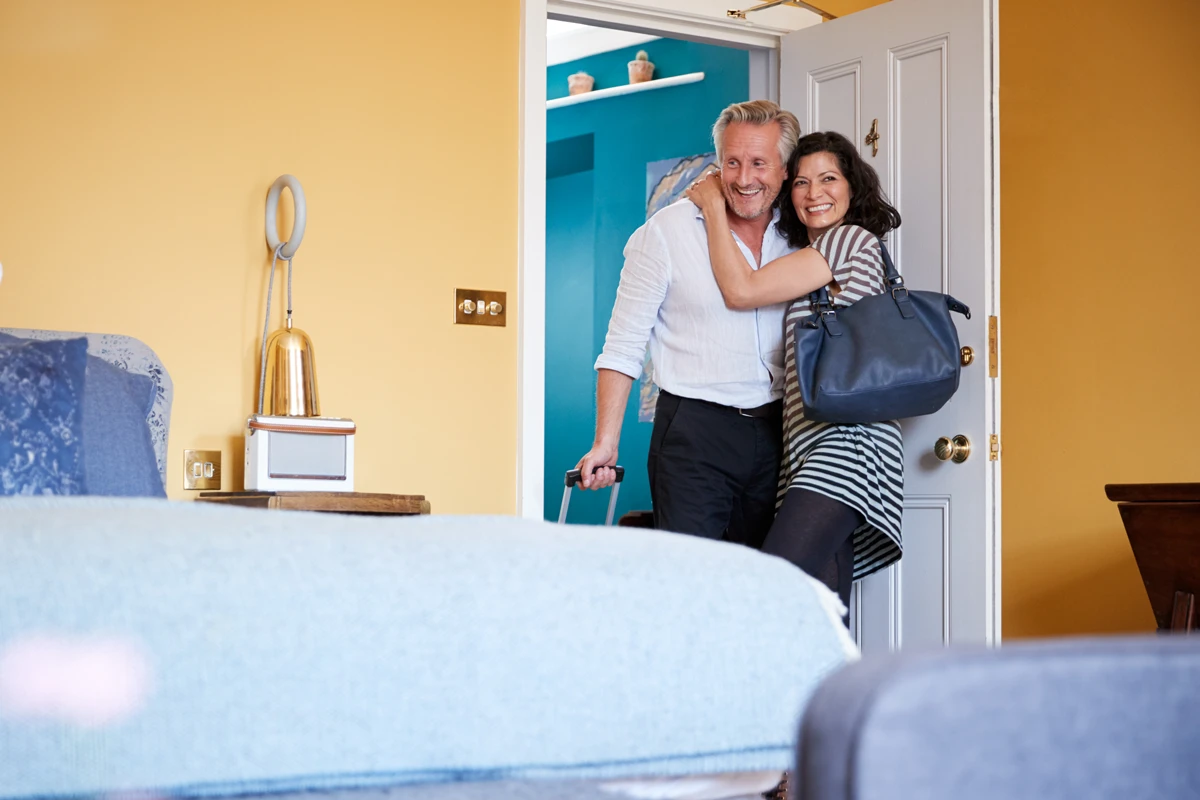 Couple smiling at home doorway with luggage