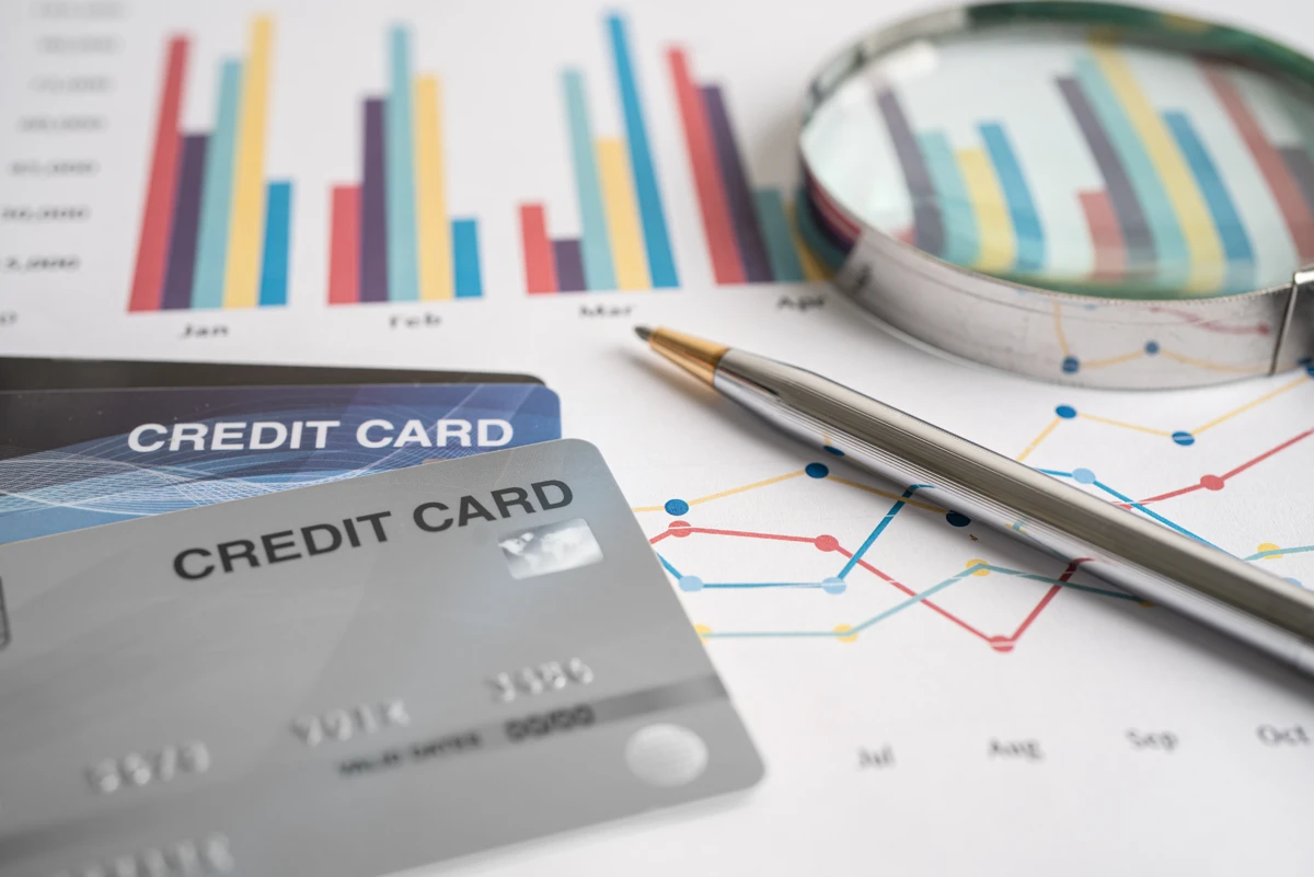 Credit cards with financial graphs, pen, and magnifying glass.