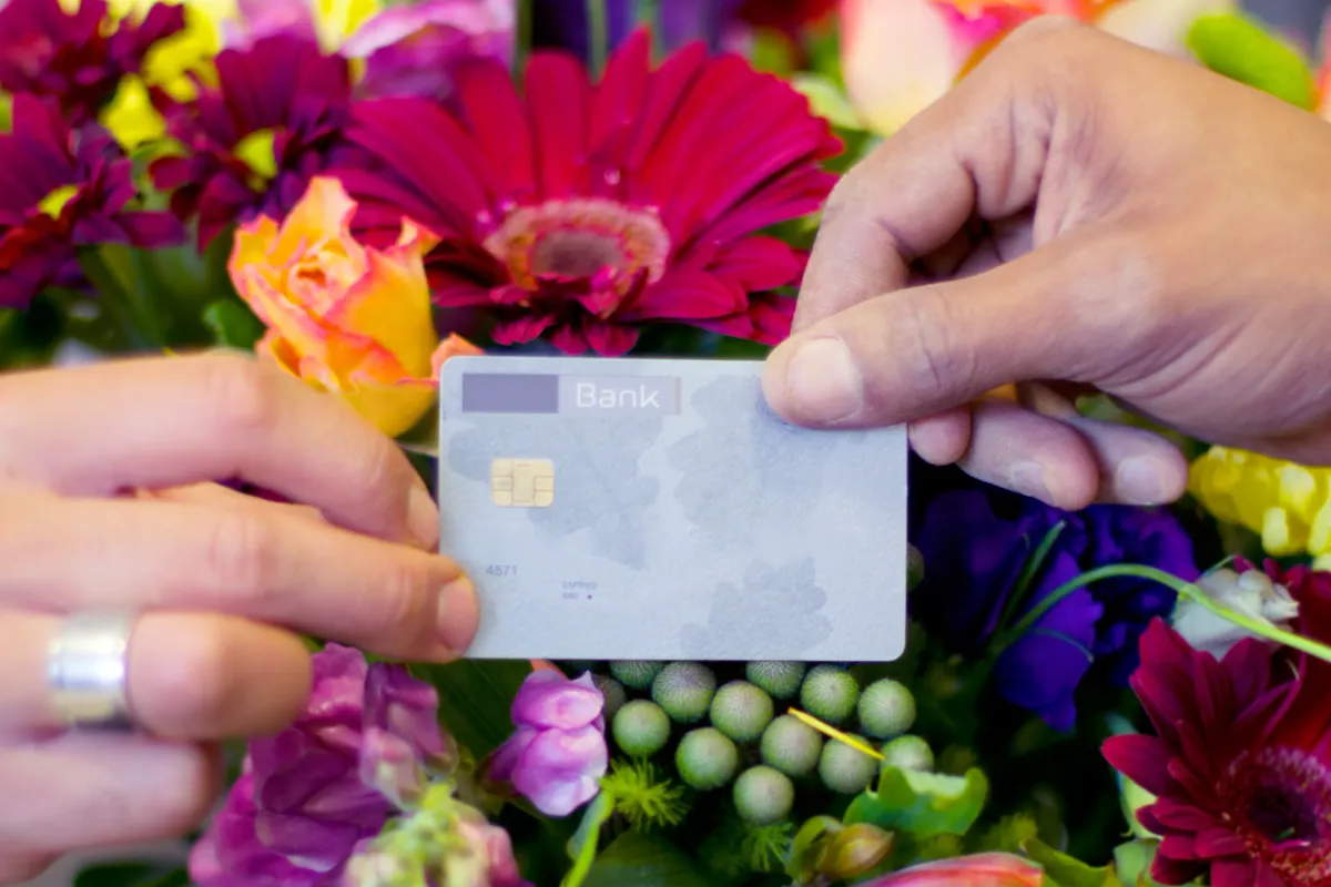 Two hands exchanging a credit card in front of a vibrant, colorful bouquet of flowers.