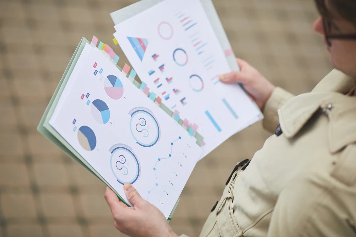 Person holding colorful printed reports with charts and graphs outdoors.