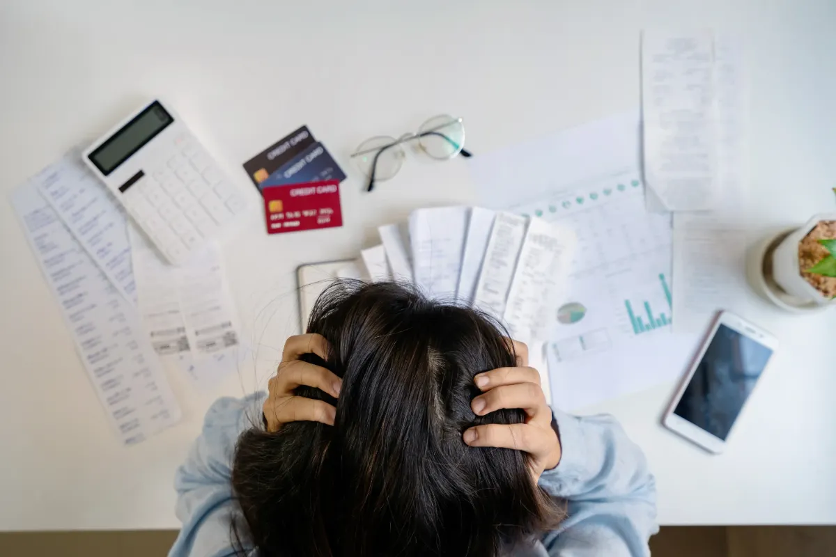 Person holding their head in frustration surrounded by bills, credit cards, and a calculator, indicating financial stress.