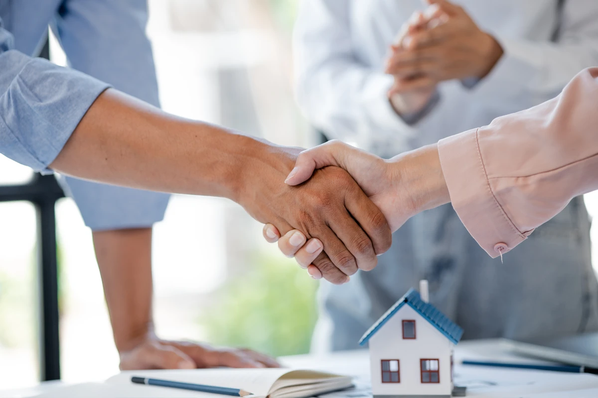 Handshake over house model at real estate meeting