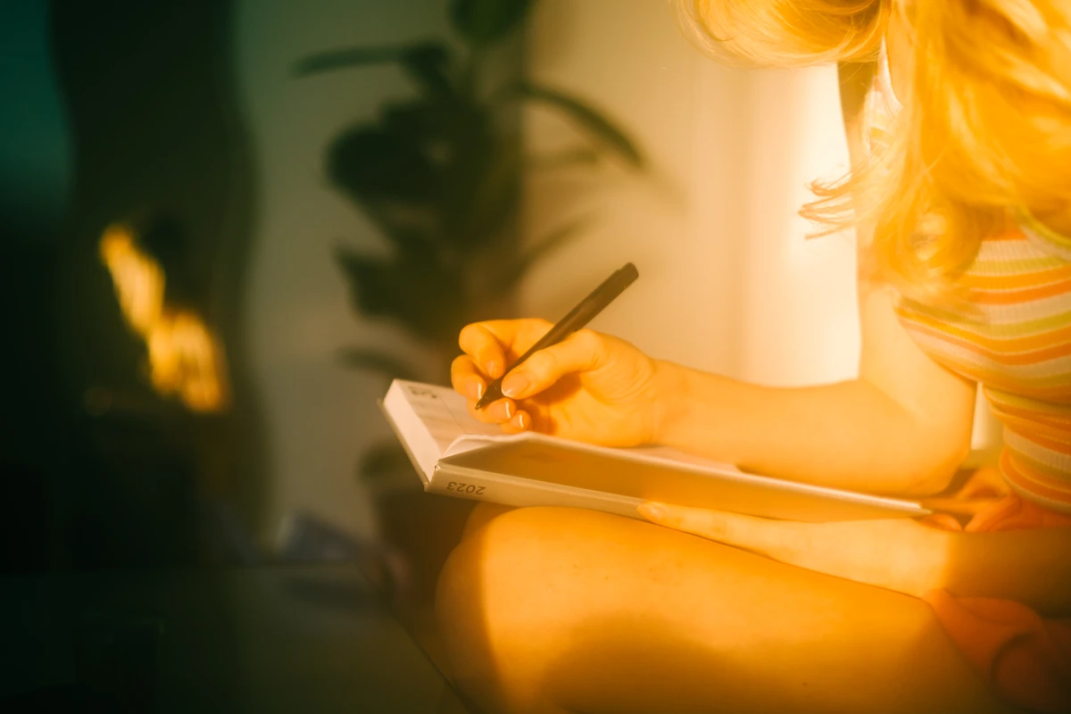 Person writing money gratitude notes in a journal in warm lighting