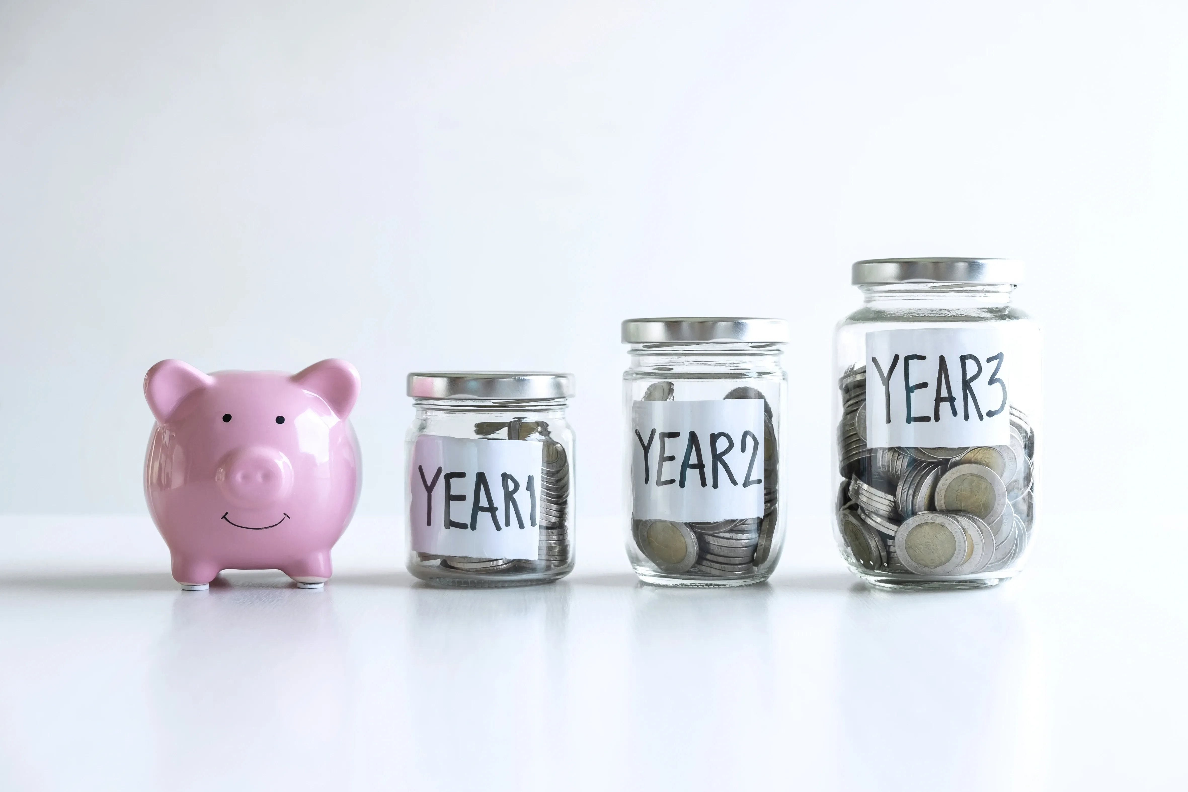 A pink piggy bank next to three jars labeled Year 1, Year 2, and Year 3, each filled with increasing amounts of coins, symbolizing growing savings over time.