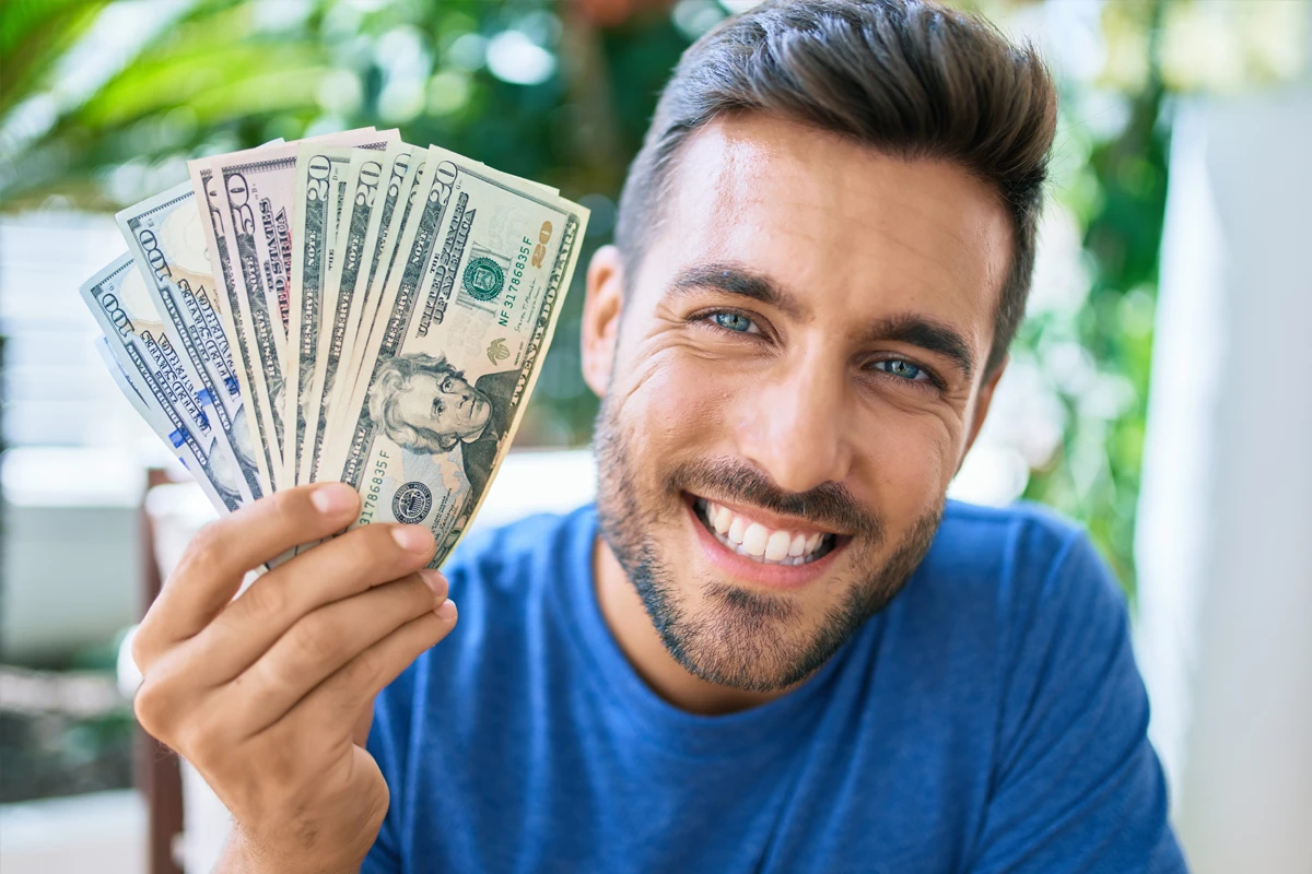 Smiling man holding multiple US dollar bills