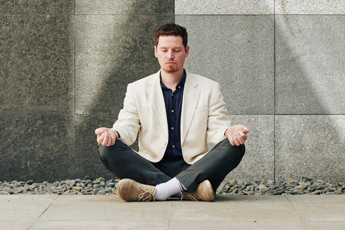 Man meditating in white blazer against stone wall.