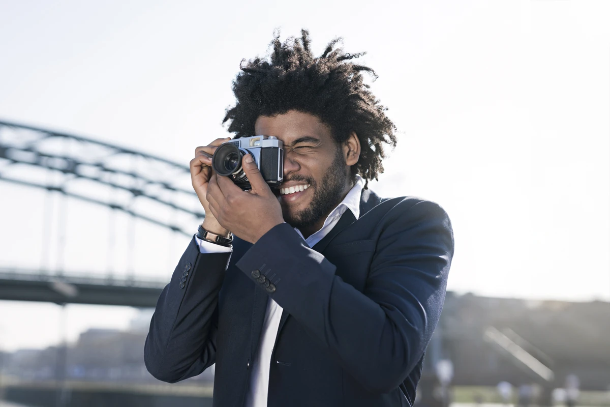 Joyful man using camera outdoors near bridge