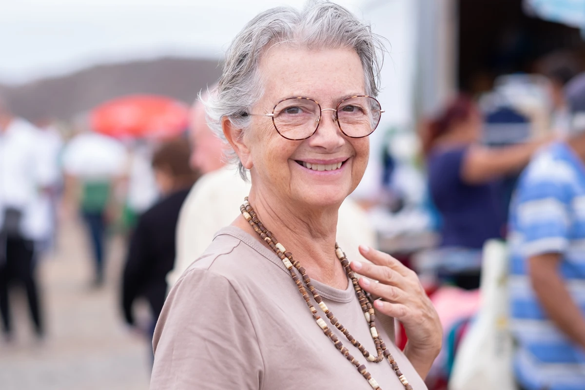 Elderly woman smiling outdoors at a crowded market