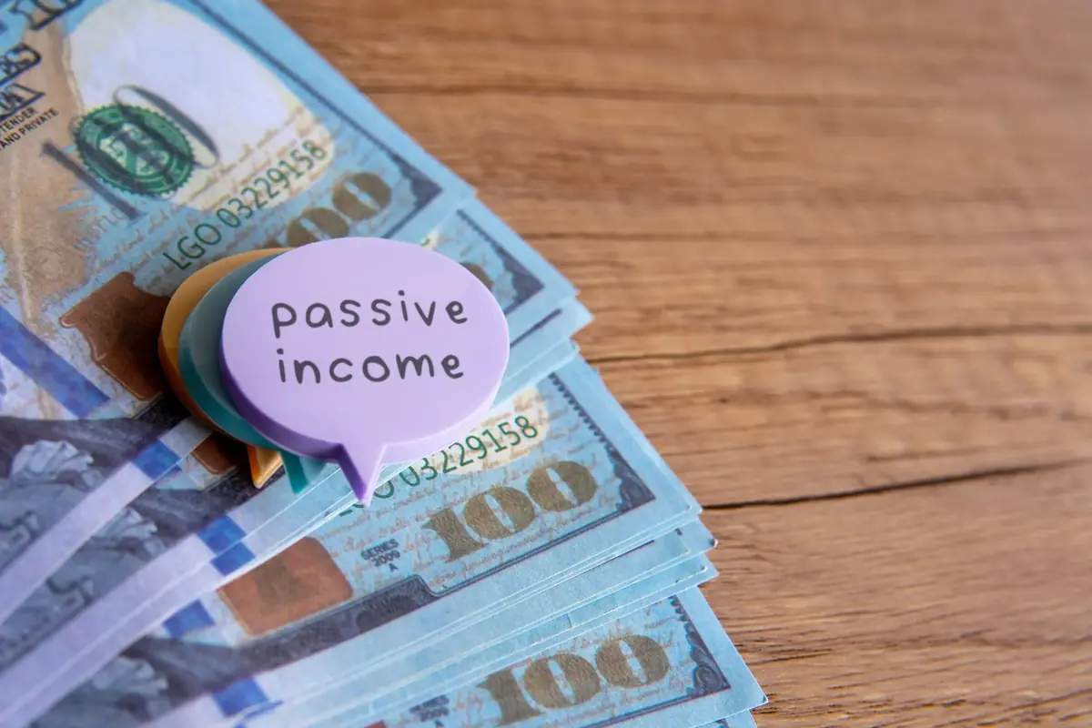 Stack of hundred-dollar bills with a purple speech bubble reading "passive income" on a wooden surface.