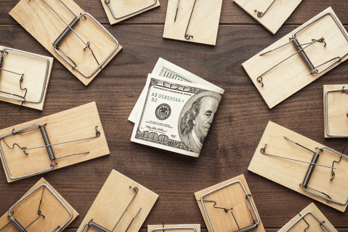 Stack of hundred-dollar bills positioned in the center of a circle of various mousetraps on a wooden surface.