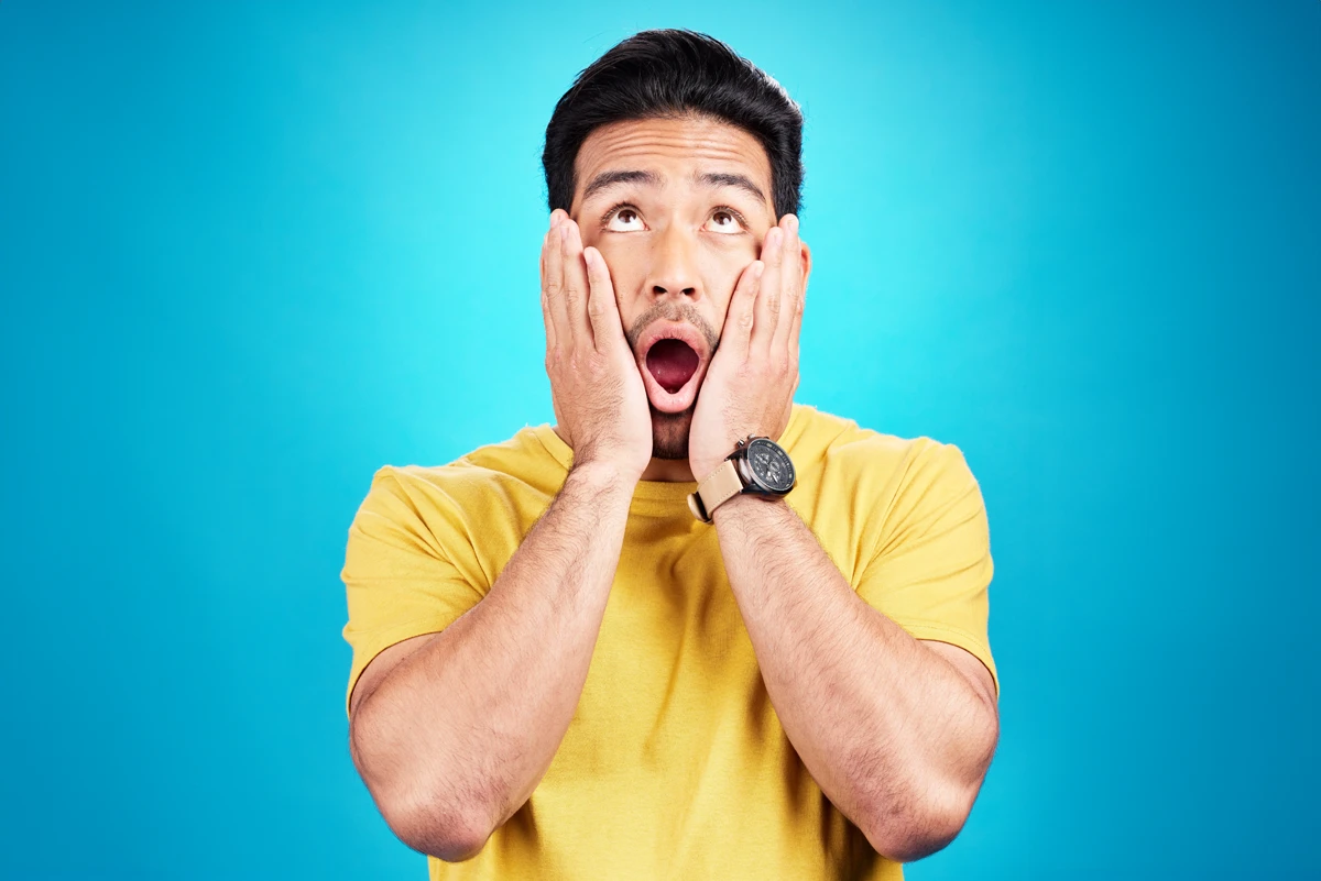 Shocked man with hands on face, blue background.