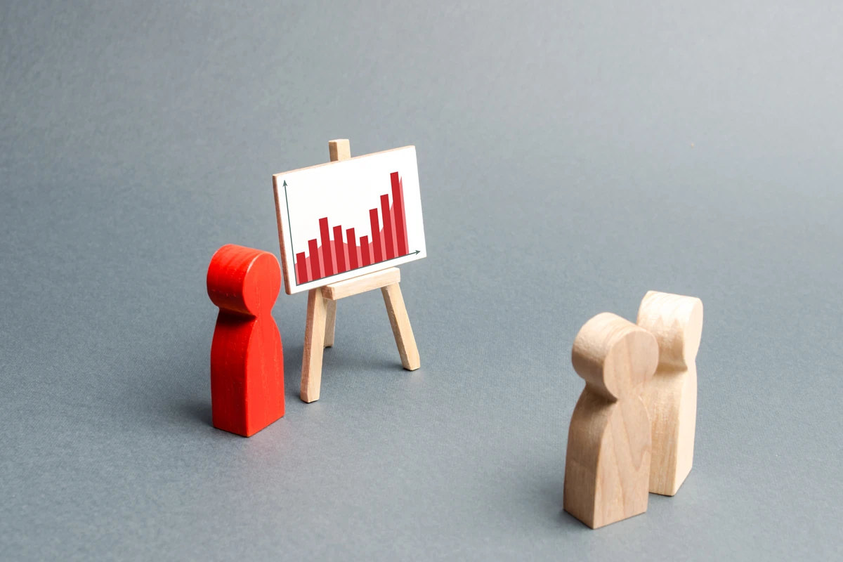 Red and wooden figures gathered around a small easel displaying a red bar graph on a gray background.