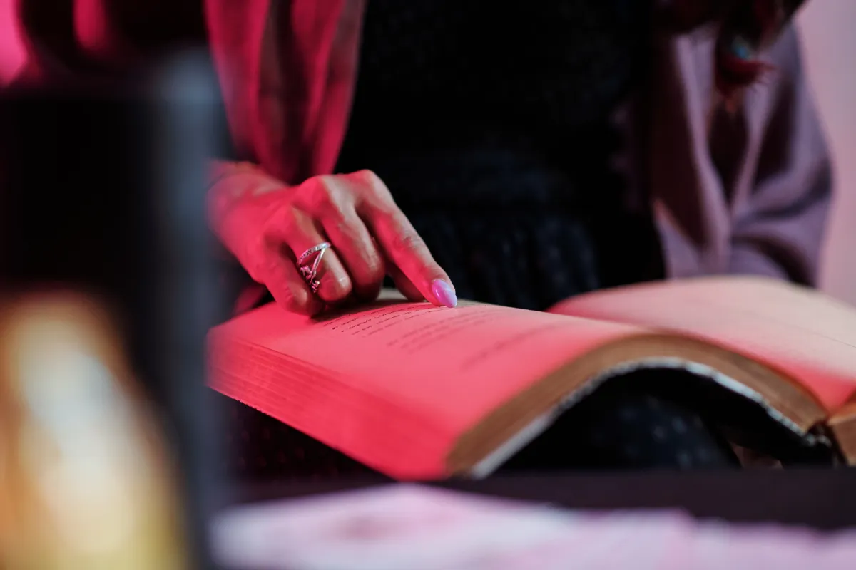 A person reading a book, gently turning the pages with a finger, illuminated by soft red lighting.