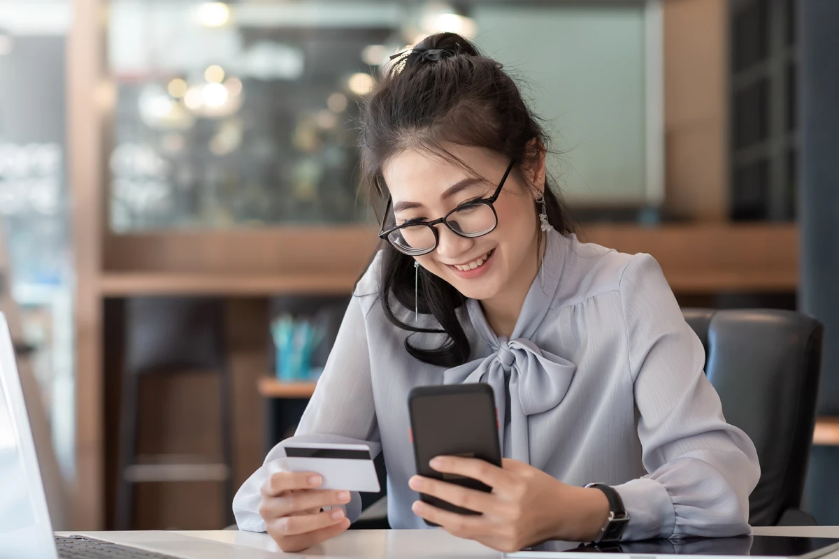 Smiling woman using smartphone and holding credit card