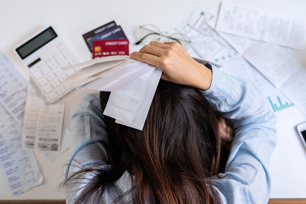 Overwhelmed woman surrounded by bills and credit cards.