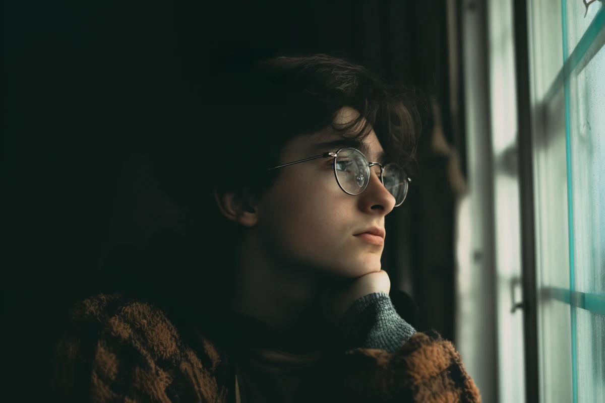 Young person pensively looking out a window