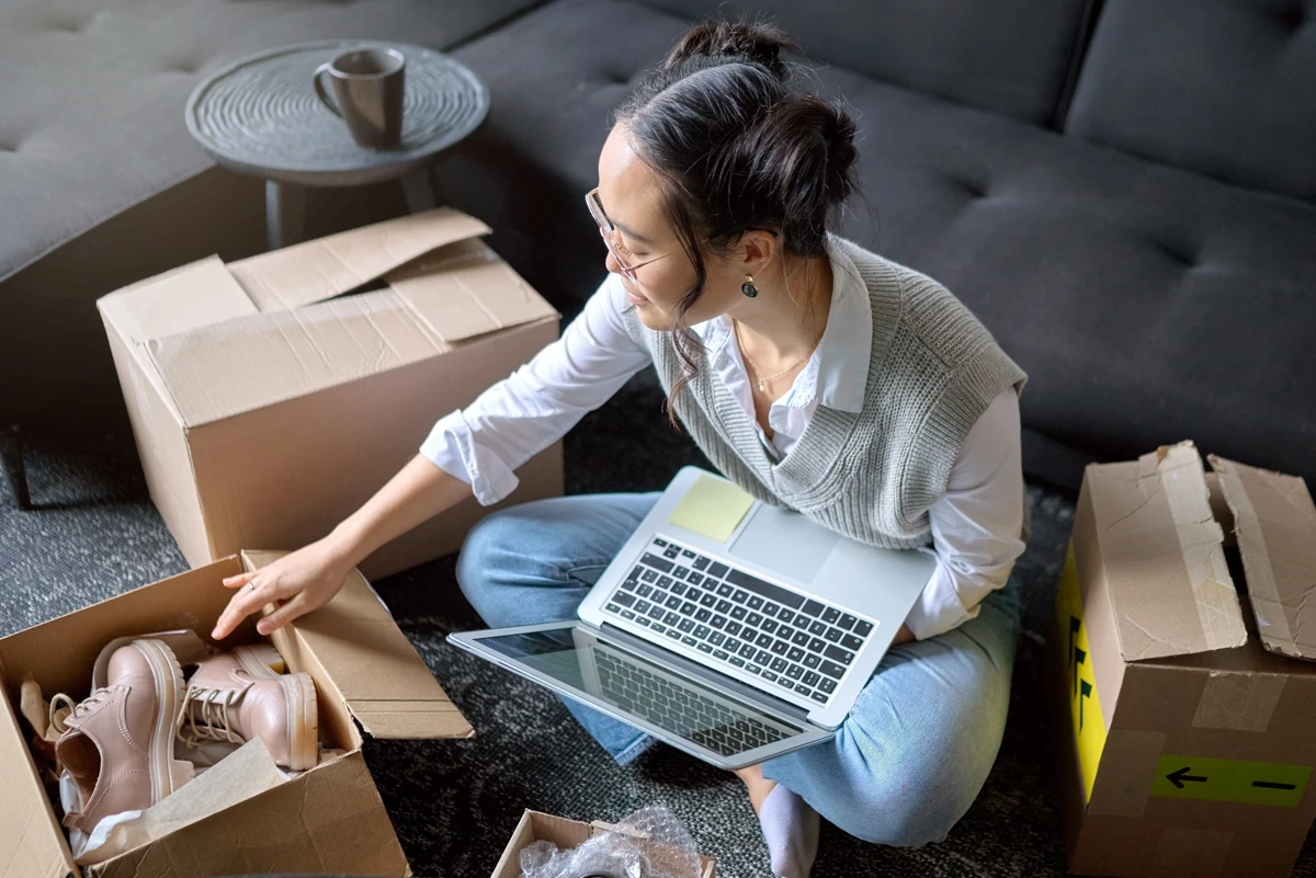 Woman unpacking shoes from box while using laptop.