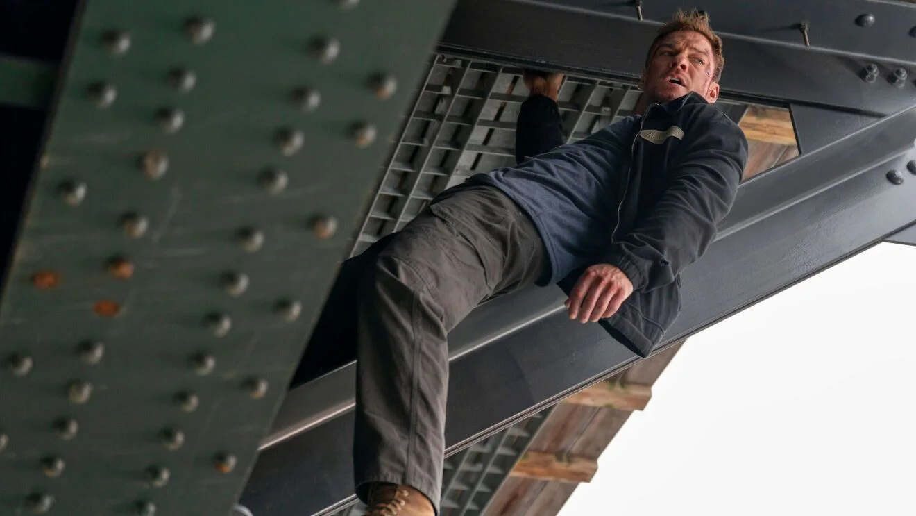 Reacher hangs beneath a steel structure.