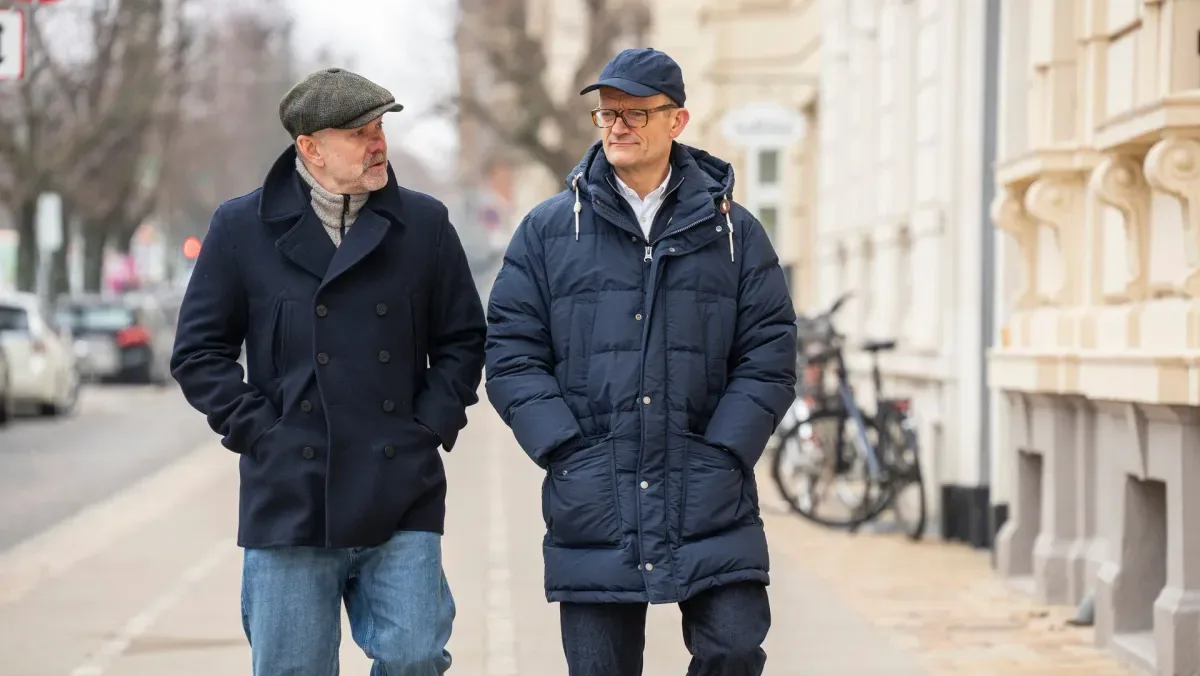 To mænd går side om side på en vinterlig bygade.