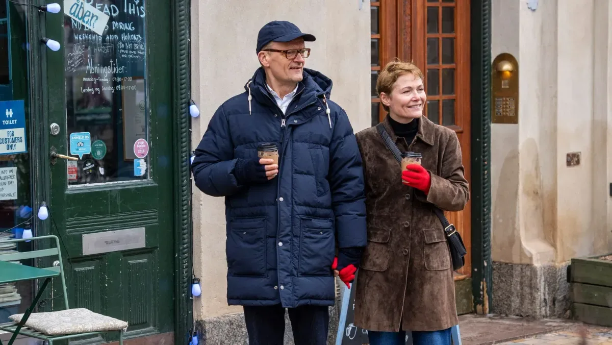 En mand og en kvinde står uden for en café med hver sin kaffekop.