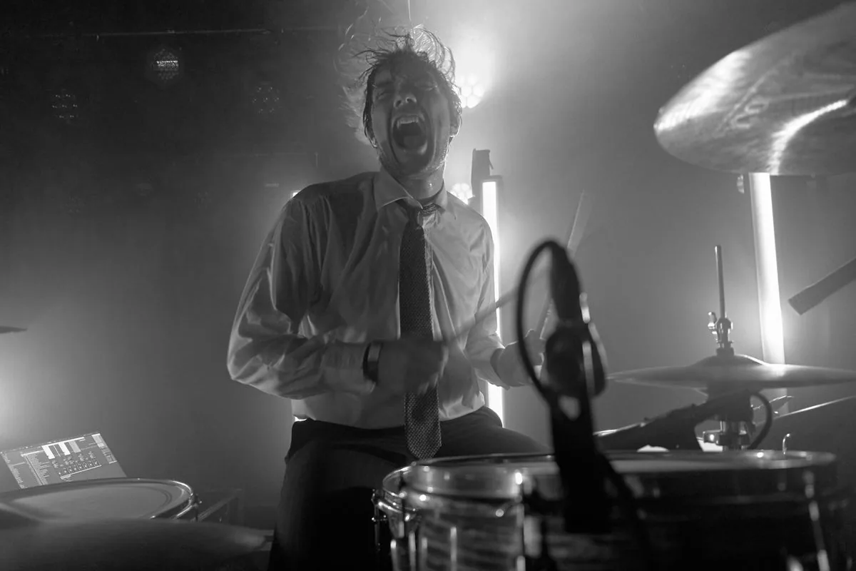 Trommeslager bag trommesættet under en intens koncert med kraftigt scenelys