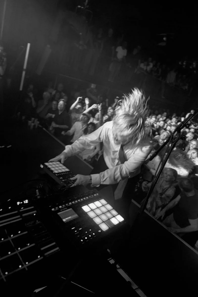 Musiker læner sig over elektronisk musikudstyr med publikum foran scenen