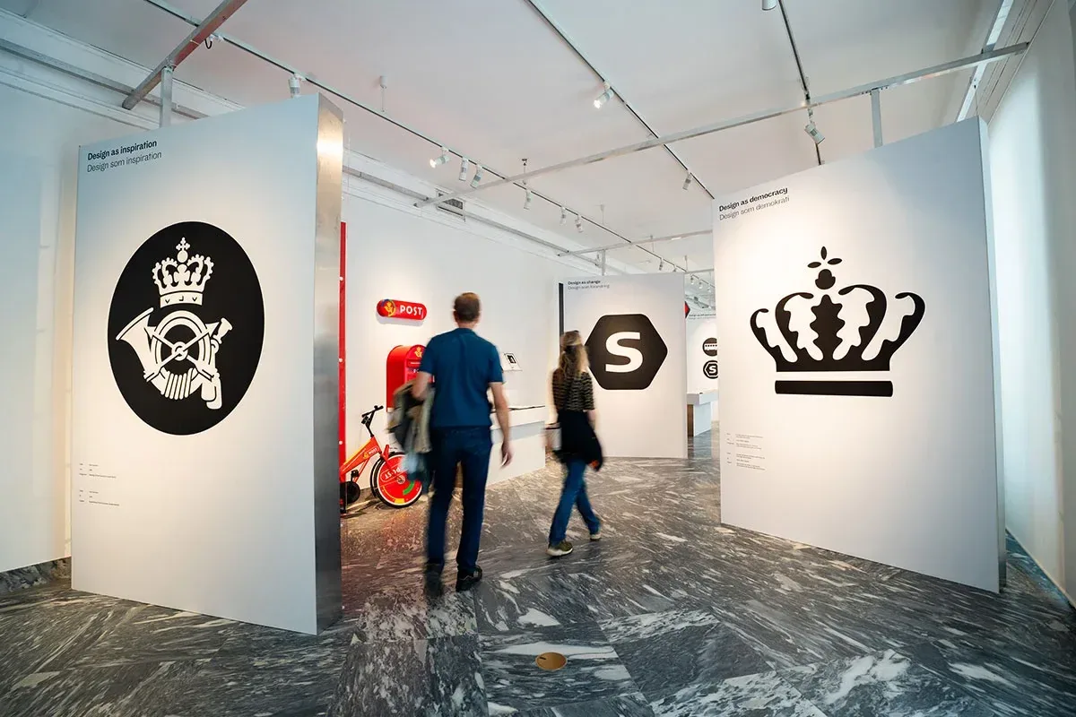 Besøgende mellem udstillingens store identitets- og logoplancher.